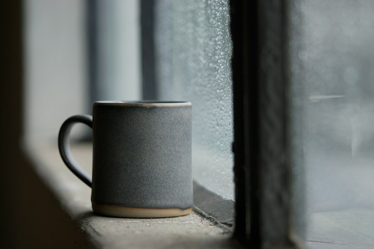 Tasse en céramique sombre posée sur le rebord d'une fenêtre en béton blanc