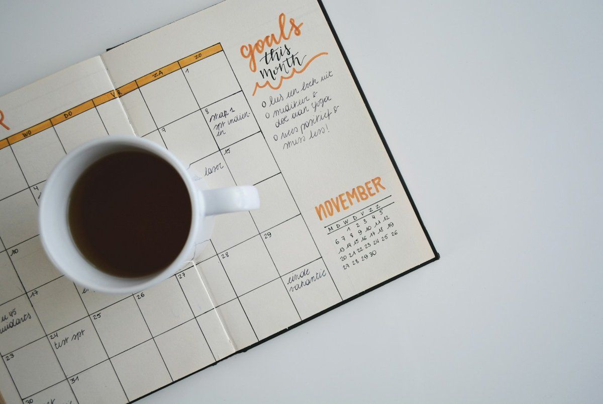 Agenda mensuel ouvert vu de dessus, avec une tasse de café posée sur les pages