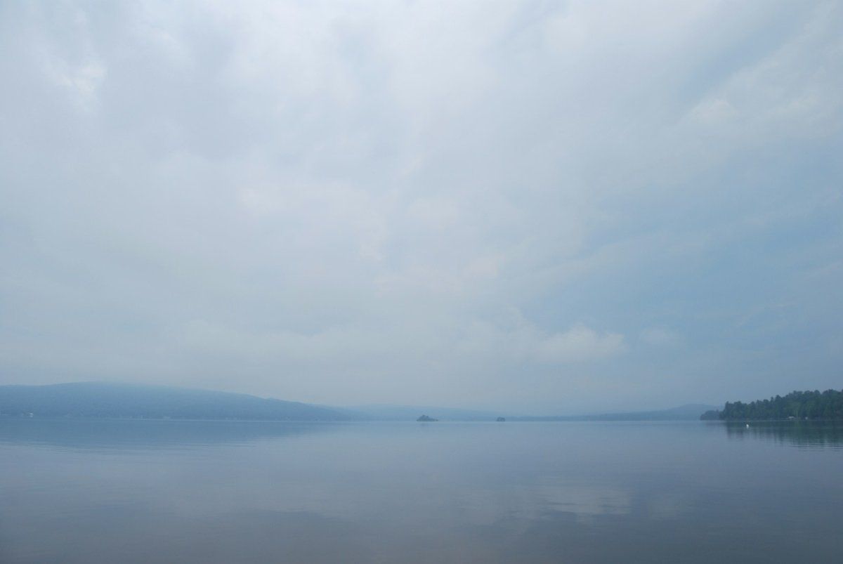 Plan d'eau entouré d'arbres sous un ciel nuageux et gris