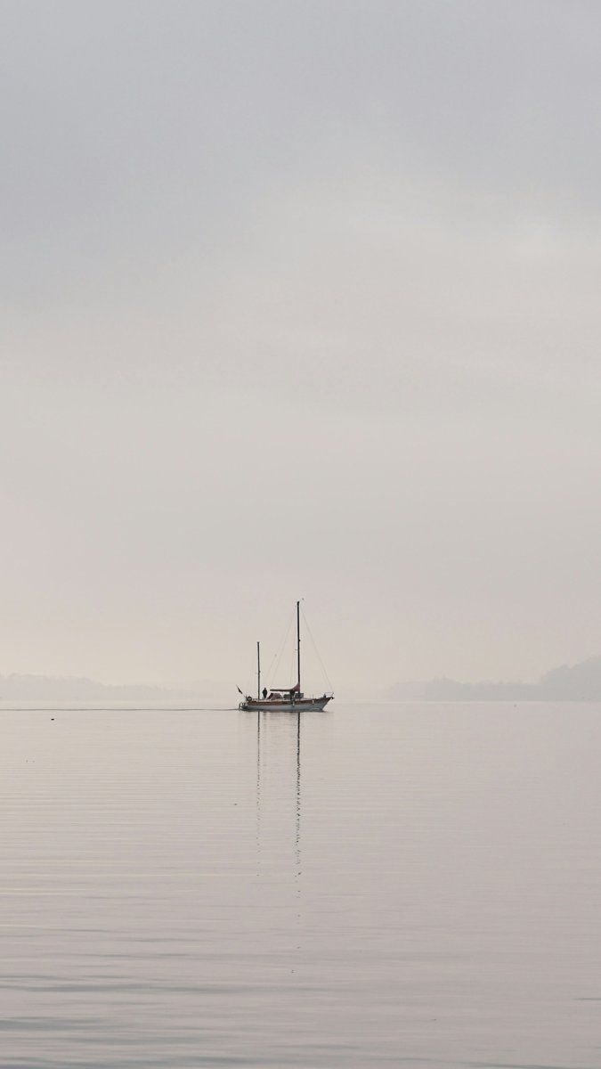 A small sailing boat on a wide grey lake under a pale sky