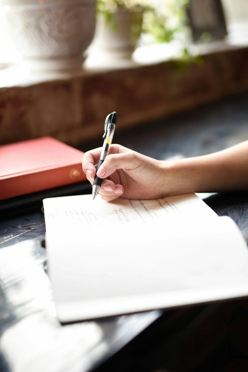 Une main qui écrit dans un carnet ouvert sur une table près d'une fenêtre