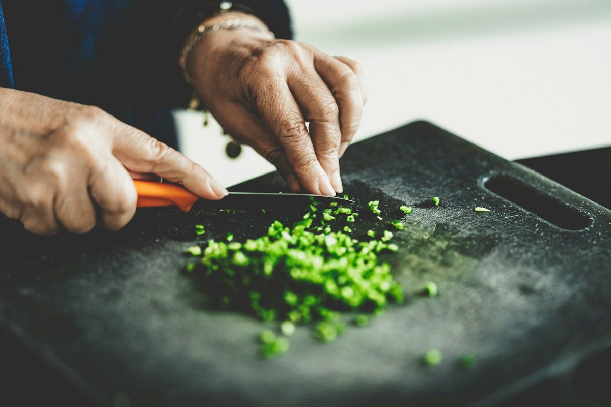 Mains qui hachent des herbes vertes sur une planche à découper noire
