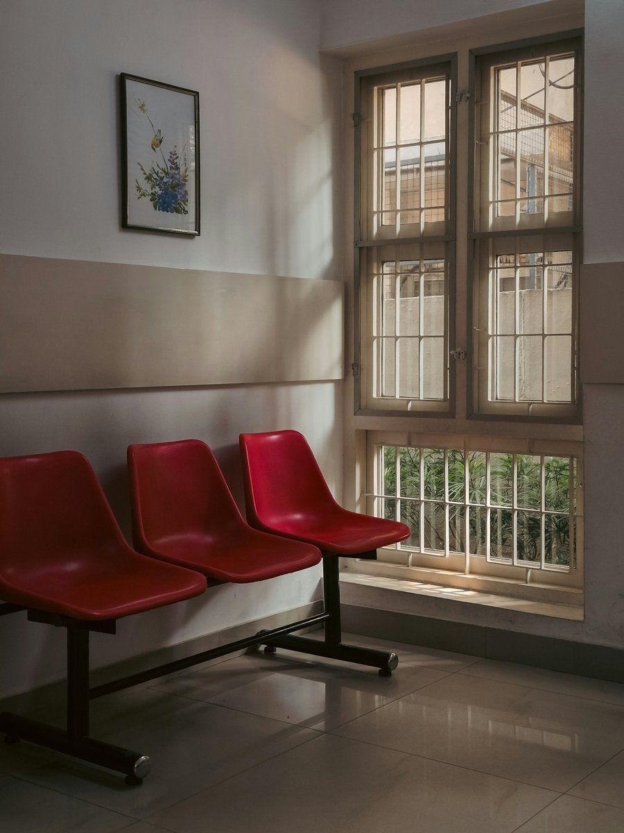 Trois chaises rouges alignées sous une fenêtre dans une salle d'attente